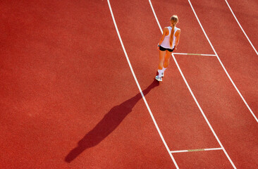young woman in sports uniform stands on the stadium treadmill, back view. sports training and...