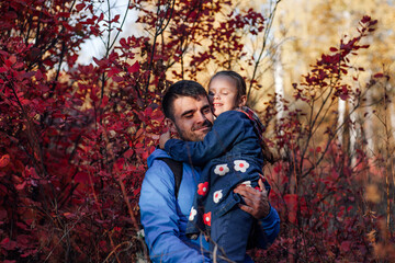 close up happy family portrait. happy father hold smiling little daughter in blue jacket at autumn forest background. 