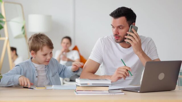 Family members at home. Spbi Funny little son bothers father talking on phone at laptop to show achievement in videogame while mother sits on couch in room