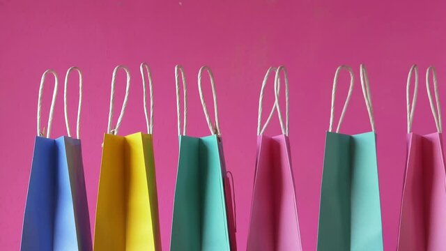 Row of colorful gift bags on pink background wide shot