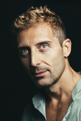 Portrait of charming man with blond hair and green and brown eyes. Black background. Green shirt.