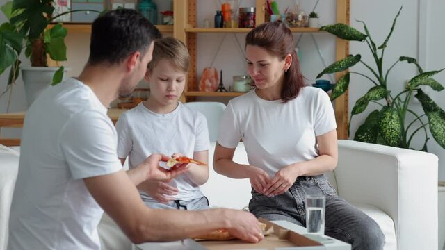 Family takeaway food at home. Spbi Bearded father gives slices of delicious hot pizza to joyful wife and little son and family enjoys weekend sitting on sofa