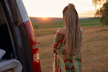 a hippie woman with long dreadlocks stands with her back to the camera wrapped in an ethnic bright...