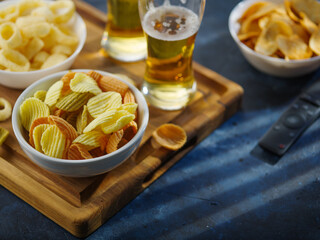 Two glasses of light beer and cold snacks - potato chips and onion rings. TV remote. Dark blue background. High angle view. Rest with friends. watching TV programs and sports matches.