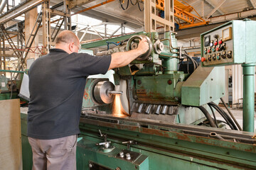 The worker controls the feed of the grinding wheel when grinding the workpiece on the machine.