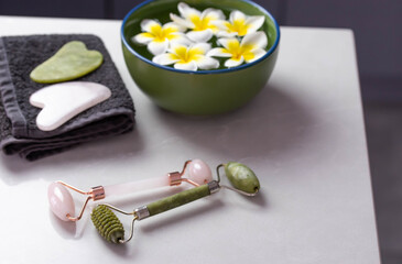 Fototapeta na wymiar Beautiful spa composition with plumeria flowers. Face roller and guasha massager. Chinese Gua Sha massage tools.