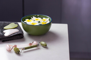 Beautiful spa composition with plumeria flowers. Face roller and guasha massager. Chinese Gua Sha massage tools.
