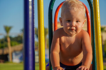 little boy with blonde hair sit on a swing and laugh