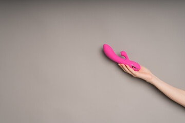 Bright pink vibrator in a female hand on an orange background. Massager for masturbation. Dildo, toys for adults