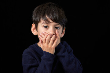 studio portrait of serious latin boy looking at the camera covering his mouth with both hands....