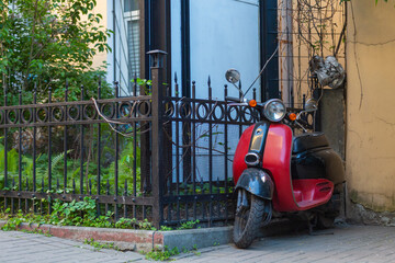 Red scooter stands on the street by the fence