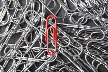 A red paper clip stands out against a textured background of silver paper clips