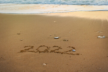 2022 Happy New Year inscription sand beach. The written text is written on yellow sand and is washed away by a wave. The concept of changing the year, the holiday. Mockup postcards copy space