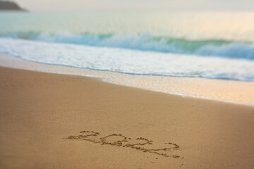 2022 Happy New Year inscription sand beach. The written text is written on yellow sand and is washed away by a wave. The concept of changing the year, the holiday. Mockup postcards copy space