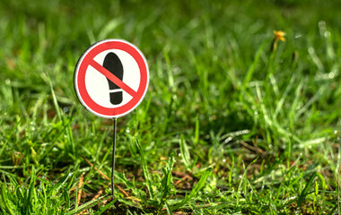 A round sign crossed out with a red stripe forbidding walking on green grass.