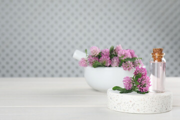 Beautiful clover flowers and bottle of essential oil on white wooden table. Space for text