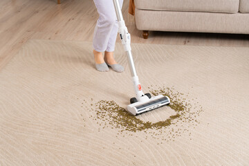 Young woman uses cordless vacuum cleaner to clean home carpet. Close-up of mung bean brush from carpet.