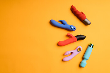 Four multi-colored dildos and a vibrator on a yellow background. Clitoral massager, sex toys