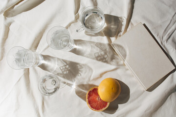 Summer sunny day flat lay table with glass, water, grapefruit,  book and fabric. Aesthetic retro minimal composition with neutral colors.