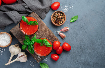 Fresh, healthy tomato juice with basil in two glasses on a dark background with ingredients. Top view, copy space.