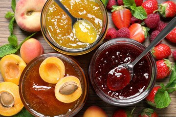 Jars with different jams and fresh fruits on wooden table, flat lay