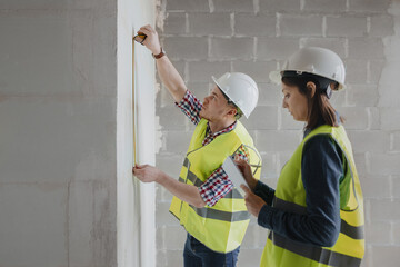 two engineers woman and man in white helmets and yellow safety vests at the construction site...