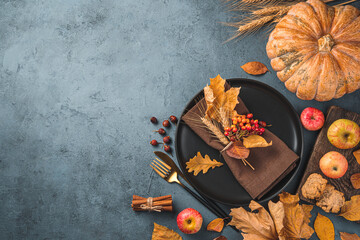 Thanksgiving day background with a black plate, napkin, cutlery, pumpkin and autumn leaves. top view, copy space.
