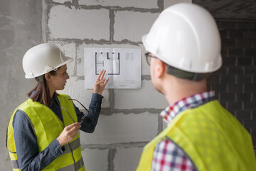 two engineers woman and man in white helmets and yellow safety vests at the construction site...