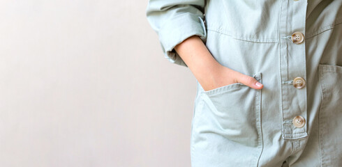 Close-up of a woman's hand in a large pocket of a working cotton light green jumpsuit with large buttons. Eco-style, natural clothing for work and home