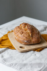 women's hands hold bread against the background of a light apron, bread with a crispy crust is beautiful and appetizing, delicious bread lies on a wooden cutting board and a kitchen knife, homemade