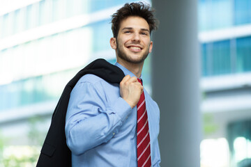 Young businessman walking and holding his jacket outdoor