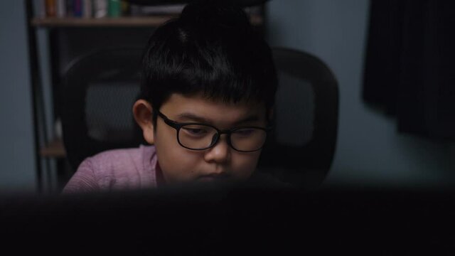 Close up face of Asian boy is playing games with a laptop in a room at night. Massively Multiplayer Online Game, child 10 years