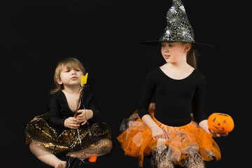 Two sisters dressed up as witches. A black blouse, a hat with cobwebs, an orange skirt. Older girl...