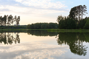 The lake, shore, grass and water surface at sunset surrounded by a dense green forest. Lake Lebyazhye, Kazan.