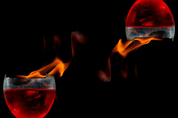 Taças de cristal cheias com bebida de cor vermelha, bordas quebradas e labaredas de fogo. 