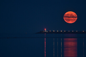 Beautiful view of rare summer full blue sturgeon Moon rising over Irish sky between Dun Laoghaire lighthouses on August 23, 2021 seen from Sandymount Beach, Dublin, Ireland. Huge Moon