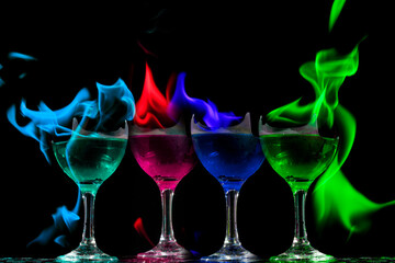 Taças vidro com liquido inflamável em chamas de cores vermelha, azul, verde e azul. 