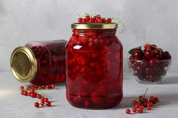 Homemade canned compote with cherries and currants in two jars on a light gray background. Organic homegrown produce