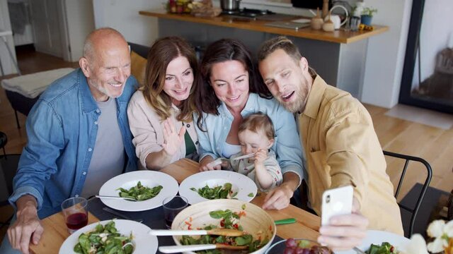 Happy multigeneration family indoors at home eating healthy lunch, taking a video.