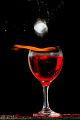 Taça de vinho tinto em chamas com uma cubo de gelo caindo dentro em um fundo escuro. 