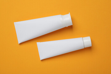 Blank tubes of toothpaste on orange background, flat lay