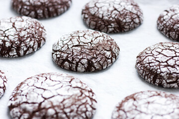 Homemade chocolate crinkle cookies in powdered sugar on a parchment paper. Food background. Selective focus.