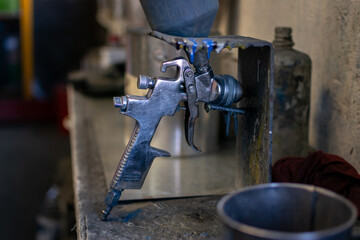 Close up of a paint gun resting on a dirty workspace