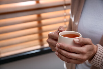Woman with cup of hot tea indoors, closeup. Cozy home atmosphere