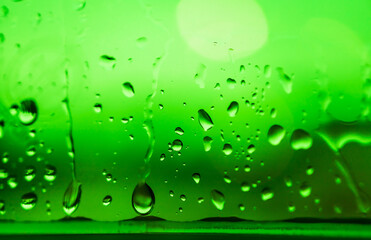 Natural water drop on window glass with green color background, depth of field. Raindrop on transparent  surface with abstract garden environment. Drops of water run down to the edge of pane, closeup.