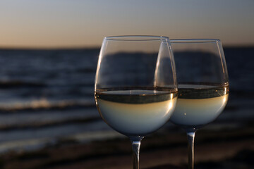 Two glasses of wine near river at sunset, closeup. Space for text