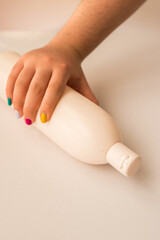 Woman with painted nails taking a skin lotion bottle from a white table 