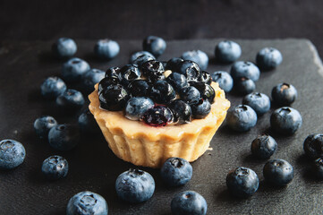 Tart with blueberries is on a black background of natural stone.