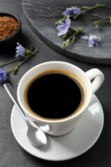 Cup of delicious chicory drink and flowers on black table