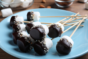 Delicious marshmallows covered with chocolate and crushed nuts on plate, closeup